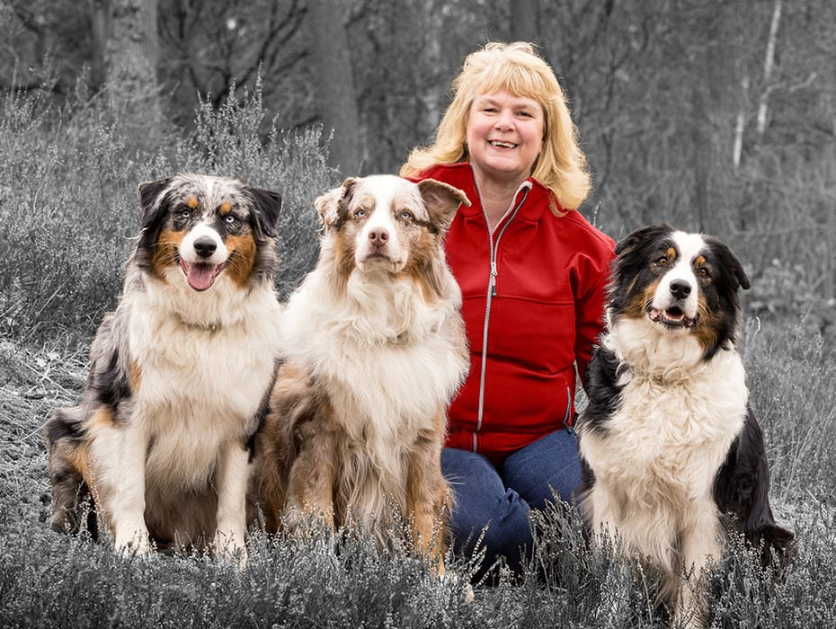 En kvinne med tre hunder sitter mot bakgrunnen av skogen