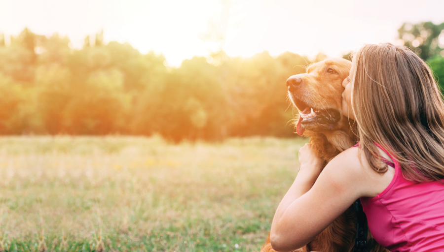 Kvinne sitter ute på en eng mens hun kysser hundens ansikt